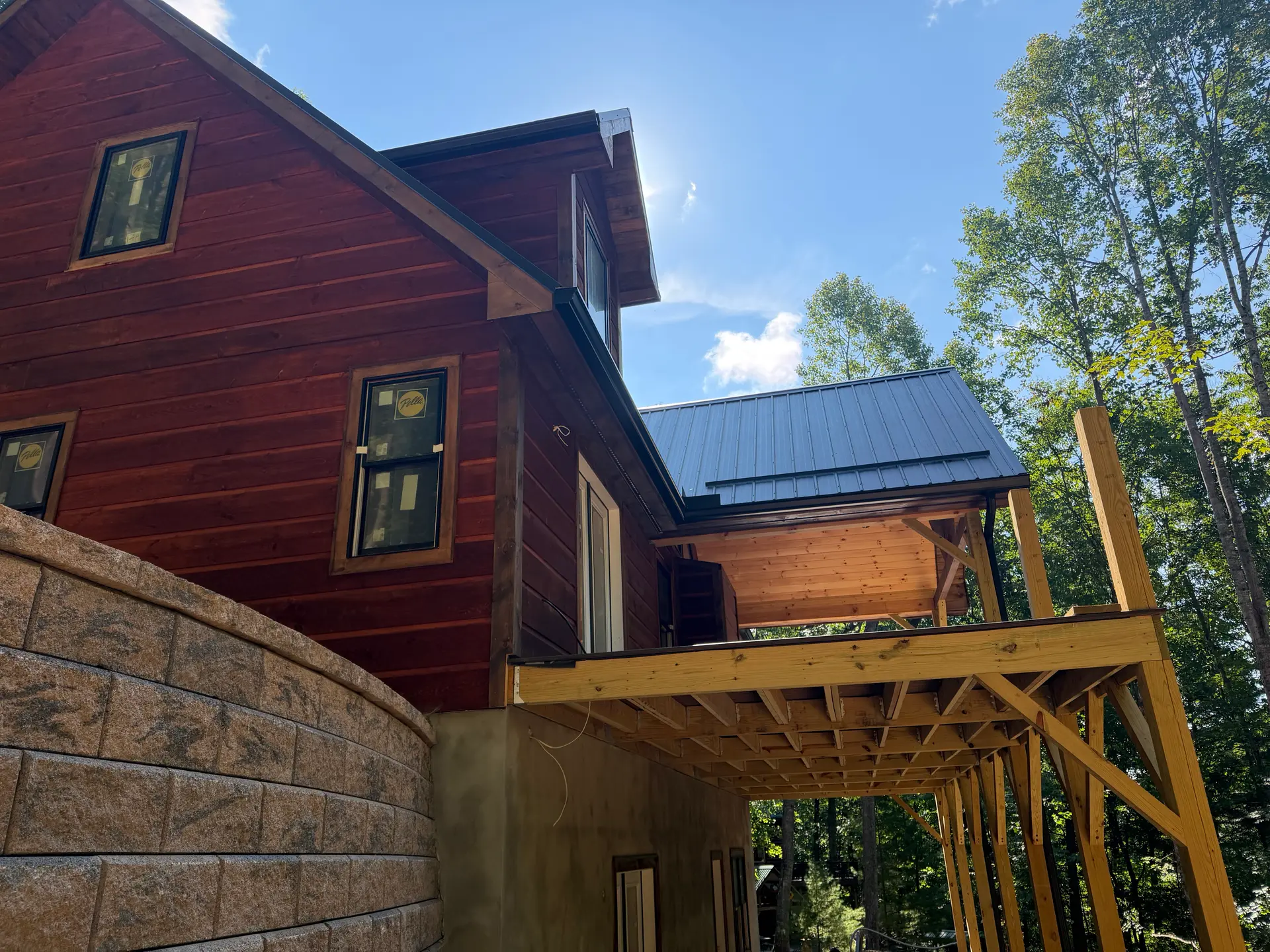 Custom residence with reddish wood siding, metal roof, and a deck frame in progress